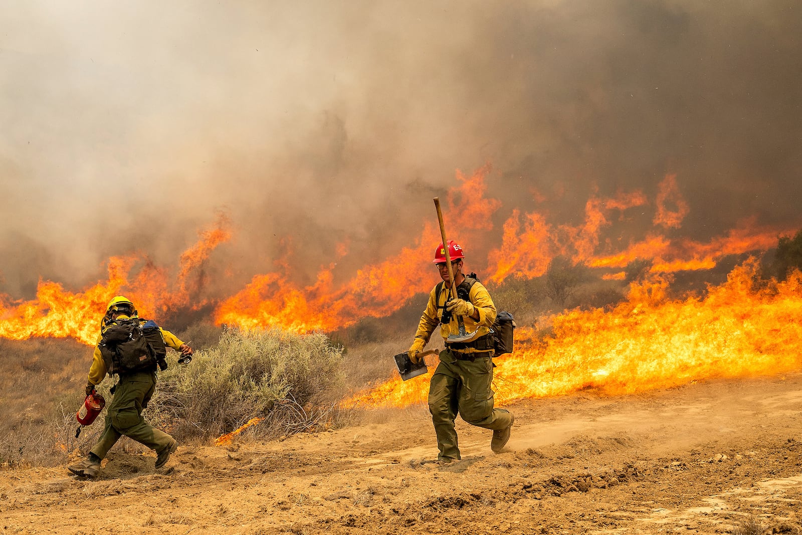 Firefighters scrambles to keep the Madre Fire from crossing a dozer line as it makes a run along Highway 166 on Thursday, July 3, 2025, in San Luis Obispo County, Calif. (AP Photo/Noah Berger)