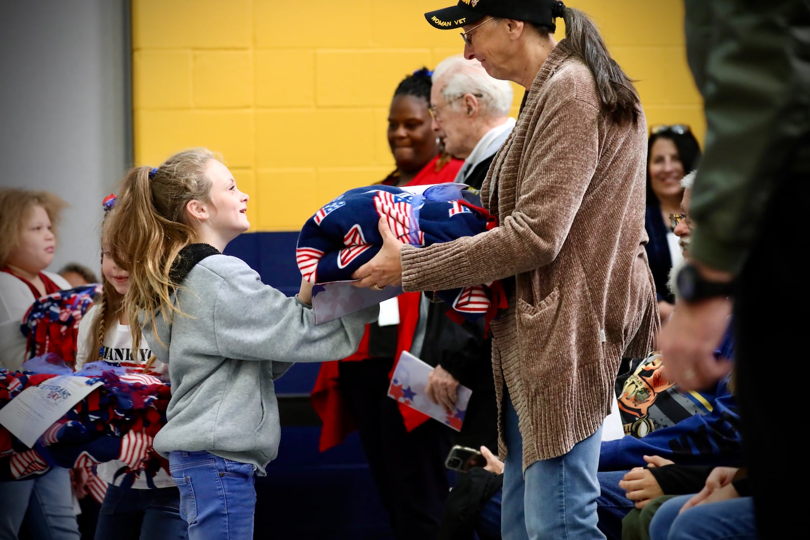 Hundreds of students in the Springfield City School District came together to honor veterans through a ceremony with special veteran guests and performances on Veterans Day, Nov. 11, 2025. Pictured are students passing out patriotic blankets to veterans at the event at Kenwood Elementary School. CONTRIBUTED