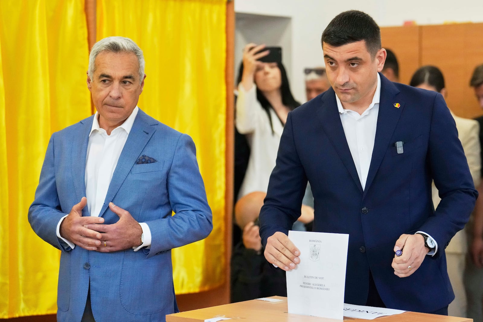 Calin Georgescu, winner of the first round of last year's annulled election, left, stands next to Presidential candidate George Simion as they cast their votes in the first round of the presidential election redo in Mogosoaia, Romania, Sunday, May 4, 2025. (AP Photo/Vadim Ghirda)
