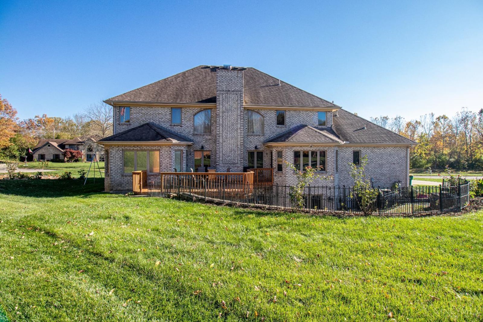 the back of the home has a wood deck with railings and a patio at the basement level with metal fencing, retaining walls and steps leading up to the yard. CONTRIBUTED