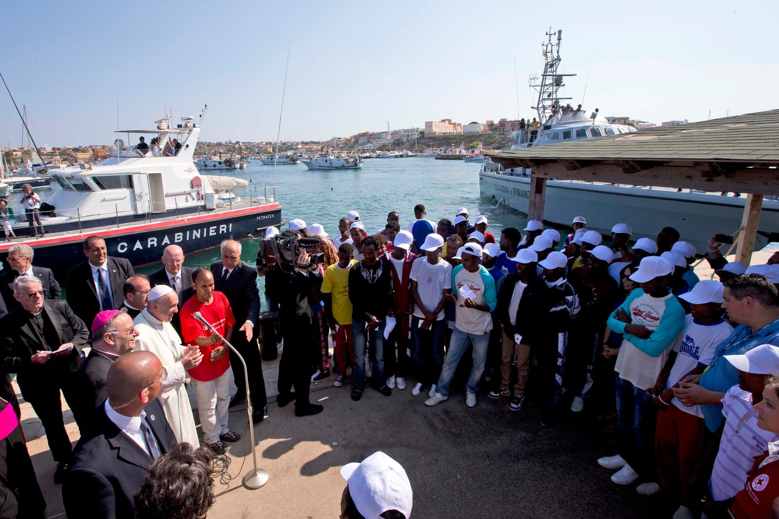 FILE - Pope Francis, left, speaks to migrants, wearing white caps, during his visit to the island of Lampedusa, southern Italy, Monday July 8, 2013. (AP Photo/Alessandra Tarantino, Pool, File)