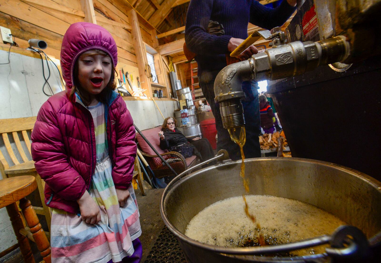 Adelaide Gobel-Lynch, a kindergartner from Academy School, watches as the syrup pours out of the boiler into a bucket to be processed during a visit to the sugar house at Lilac Ridge Farm in Brattleboro, Vt., on Friday, March 14, 2025. (Kristopher Radder/The Brattleboro Reformer via AP)