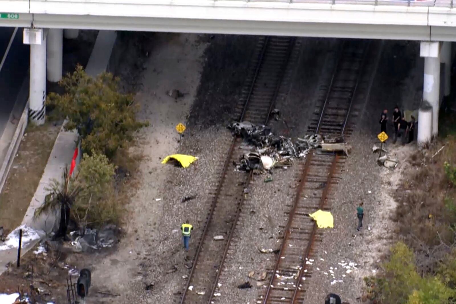 In this image taken from video provided by WSVN-TV, emergency personnel respond to the area where a small plane crashed on the railroad tracks beneath the overpass near Interstate 95 in Boca Raton, Fla., Friday, April 11, 2025. (WSVN-TV via AP)