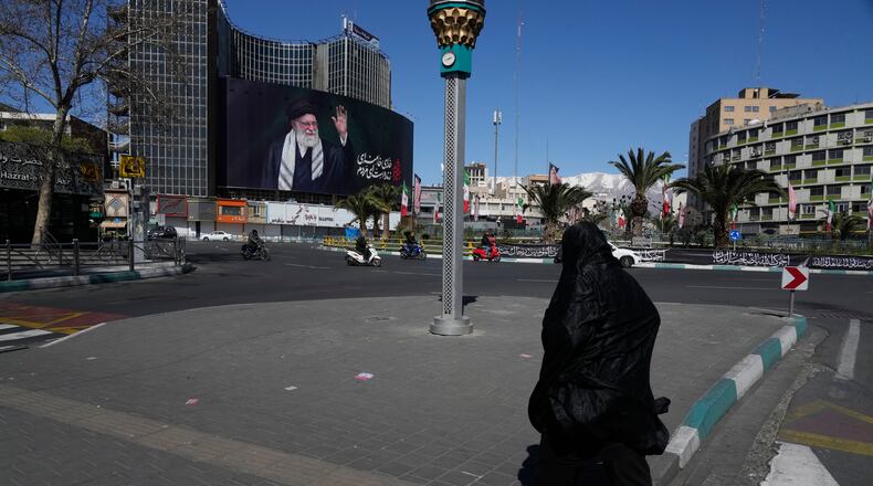 A woman crosses almost deserted square with a billboard at rear showing a portrait of the late Iranian Supreme Leader Ayatollah Ali Khamenei, who was killed in the U.S.–Israeli military campaign, in Tehran, Iran, Tuesday, March 3, 2026. (AP Photo/Vahid Salemi)
