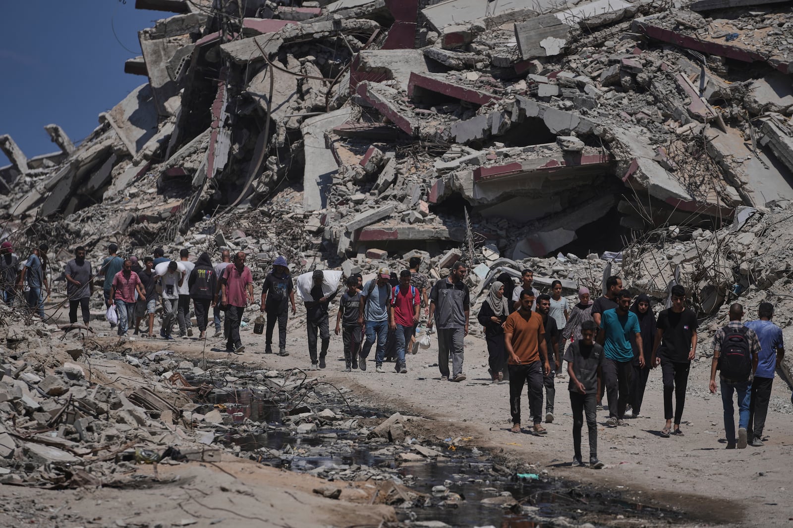 Palestinians carry sacks of humanitarian aid unloaded from trucks convoy that had been heading to Gaza City, in the northern Gaza Strip Sunday, July 20, 2025. (AP Photo/Jehad Alshrafi)