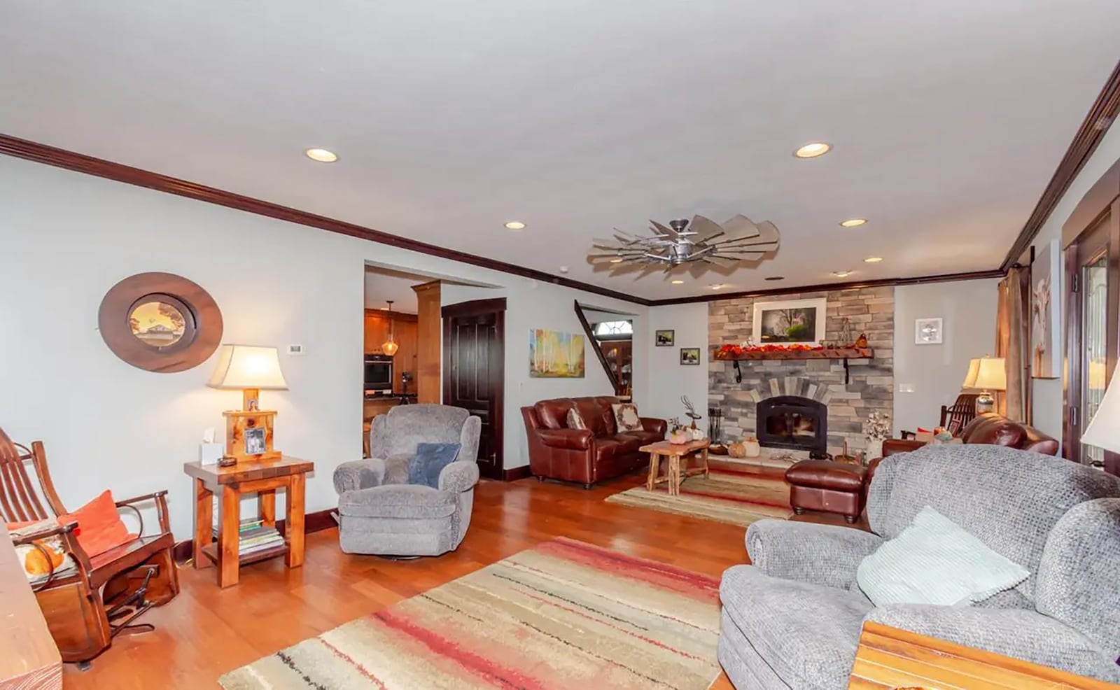 the living room has hardwood floors and crown molding, recessed lighting and a ceiling fan. There is a woodburning stone floor to ceiling fireplace with wood mantel at one end.