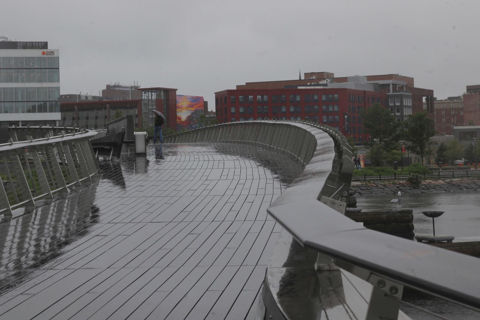 A man walks in the rain across a pedestrian bridge in Providence, R.I. (AP Photo/Kimberlee Kruesi)