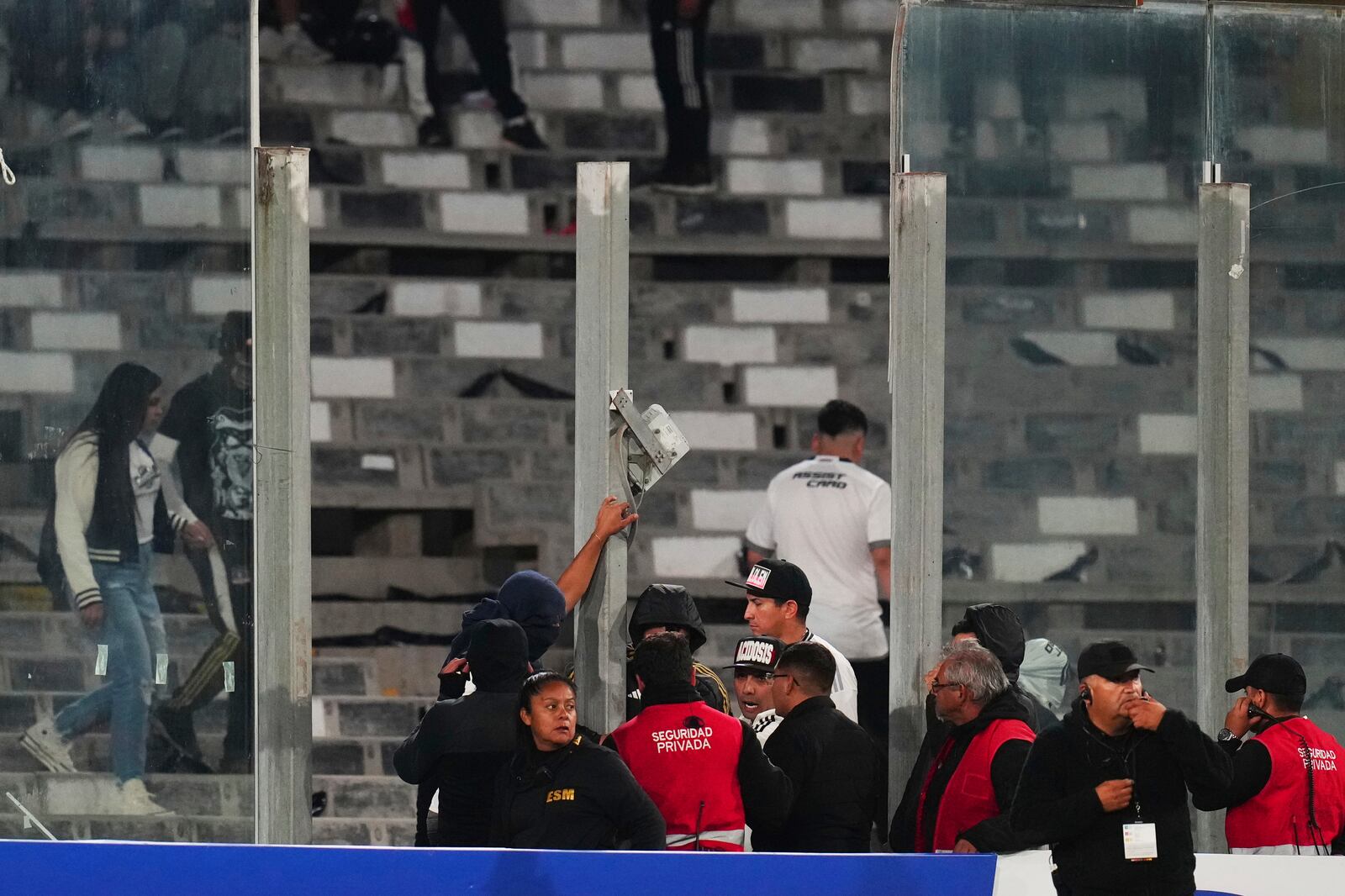 Security stewards confront fans after glass panels were broken and people invaded the field during a Copa Libertadores Group E soccer match against Brazil's Fortaleza at Monumental Stadium in Santiago, Chile, Thursday, April 10, 2025. (AP Photo/Esteban Felix)