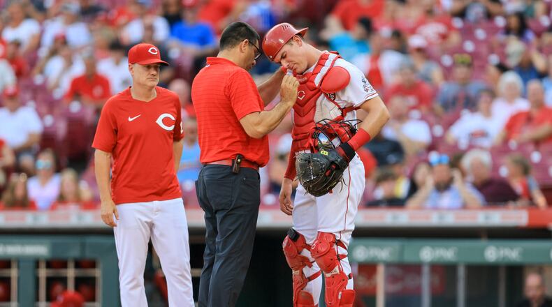 Cincinnati Reds' Tyler Stephenson, right, is checked by assistant athletic trainer Tomas Vera during the first inning of the team's baseball game against the St. Louis Cardinals in Cincinnati, Friday, July 22, 2022. (AP Photo/Aaron Doster)