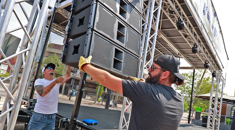 Derek Snowden, left, and Dana Akers, owners of Woolly Stage Company, raise a bank of speakers up Friday, May 19, 2023 as they set up their stage in front of the Springfield COhatch for IndieCraft 2023, which starts Friday evening and continues Saturday. BILL LACKEY/STAFF