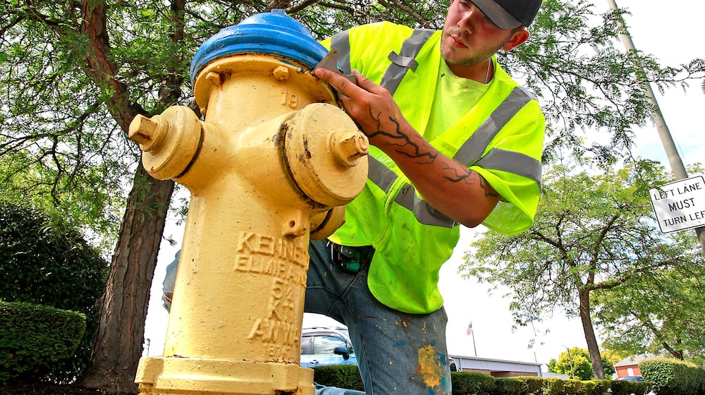 A file photo of Josh White, a city of Springfield Utilities Department seasonal employee, scraping all the loose paint off a fire hydrant along West Main Street before he paints it on July 30, 2024. BILL LACKEY/STAFF