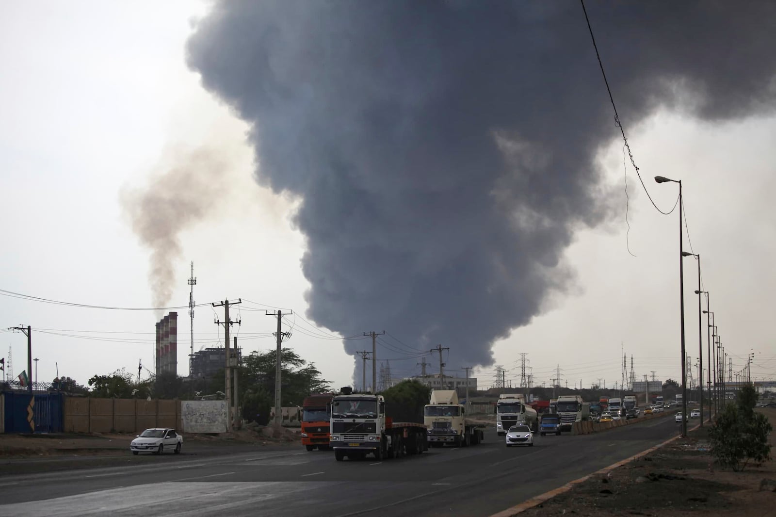 In this photo provided by Islamic Republic News Agency, IRNA, a black smoke rises in the sky as vehicles drive on the road after a massive explosion rocked a port near the southern port city of Bandar Abbas, Iran, Saturday, April 26, 2025. (Mohammad Rasoul Moradi/IRNA via AP)