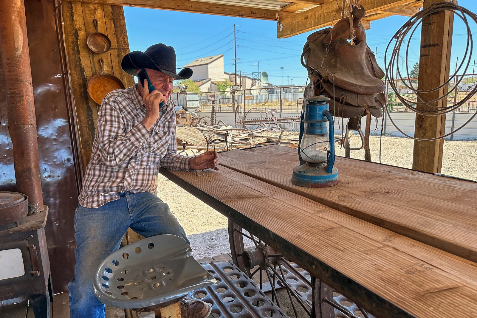 Rancher Brantley Baird takes a phone call while sitting in the shade at his pioneer museum in Joseph City, Ariz., Wednesday, April 23, 2025. (AP Photo/Susan Montoya Bryan)