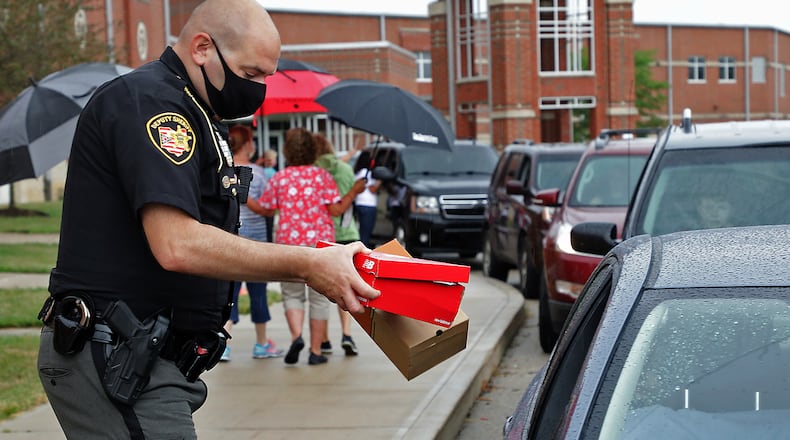 Clark County Sheriff's Deputy John Loney hands out boxes of shoes for children during the Shoes 4 the Shoeless drive thru event at Tecumseh High School Wednesday morning. BILL LACKEY/STAFF