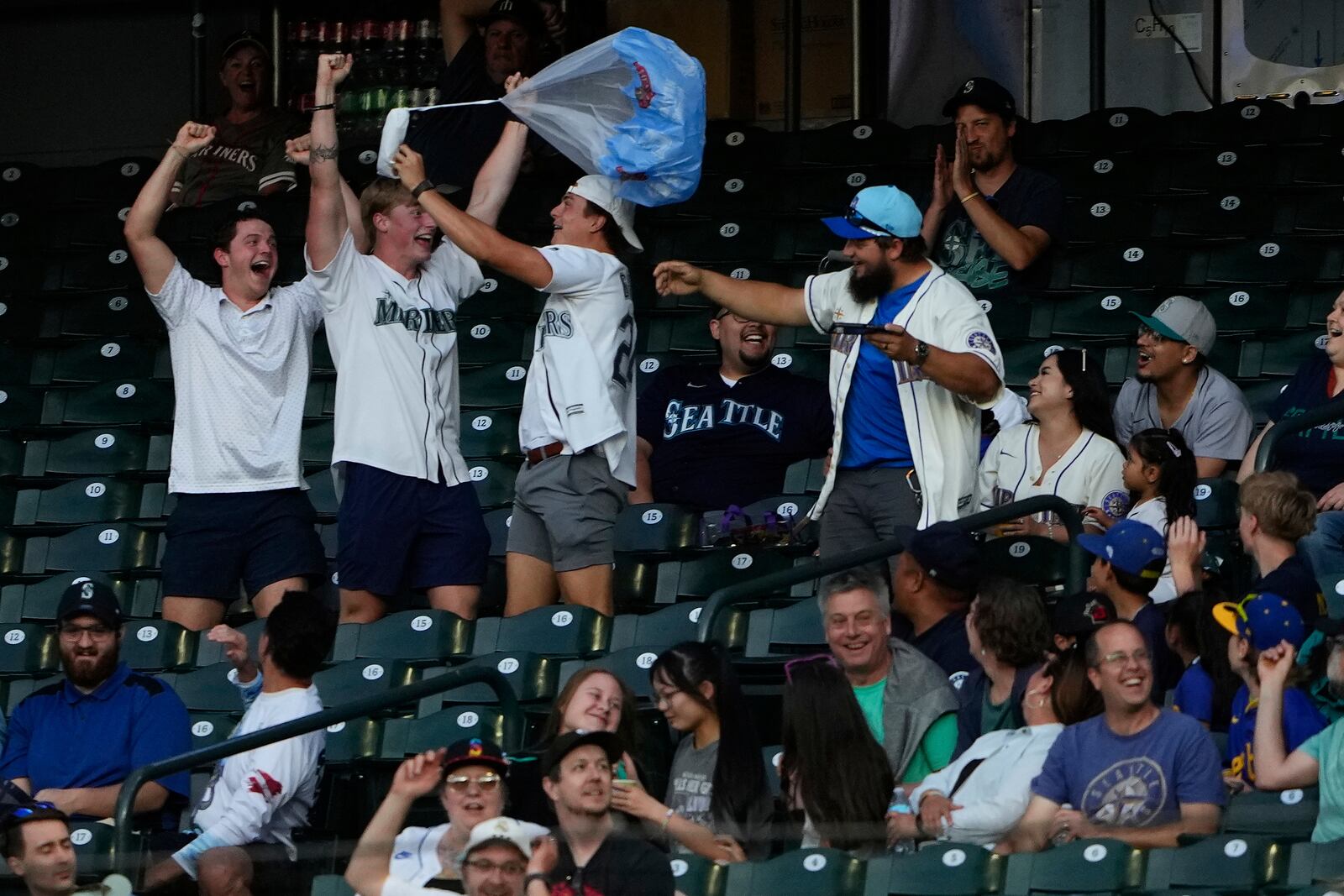 Fans react after catching a hot dog on a parachute during a baseball game between the Seattle Mariners and the Kansas City Royals, Tuesday, July 1, 2025, in Seattle. (AP Photo/Lindsey Wasson)