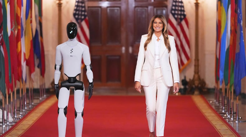 First lady Melania Trump arrives, accompanied by a robot, to attend the "Fostering the Future Together Global Coalition Summit," with other first spouses, at the White House, Wednesday, March 25, 2026, in Washington. (AP Photo/Jacquelyn Martin)