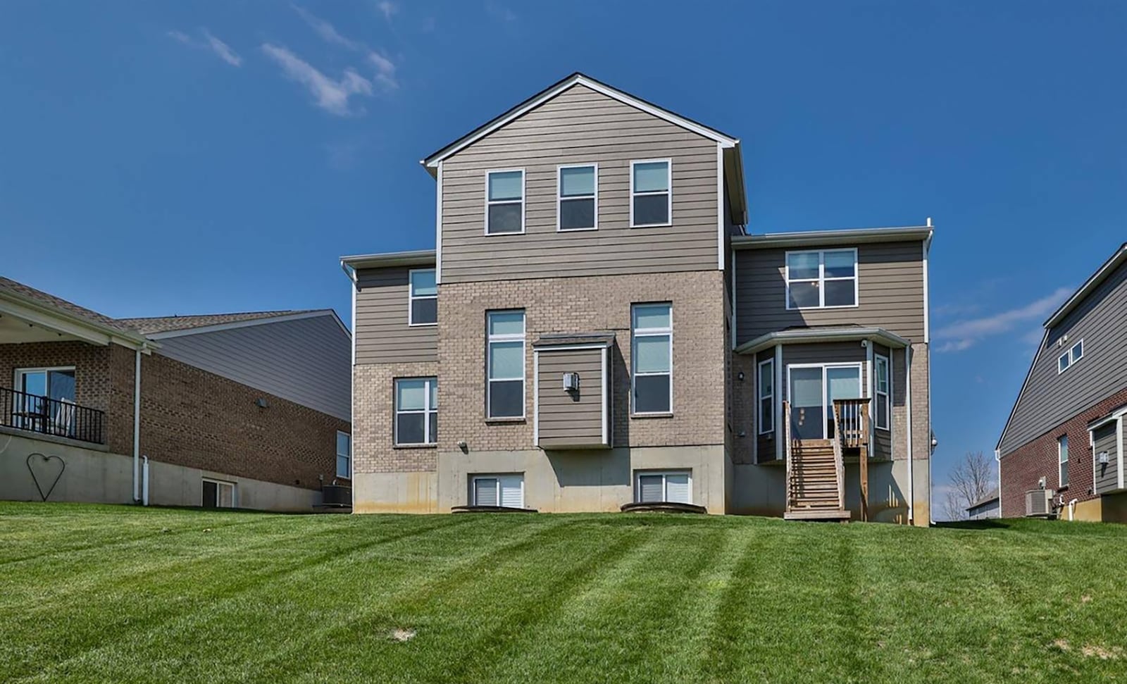 The rear of the home shows the available daylight windows in the unfinished basement. There is a wood deck with steps off the kitchen.