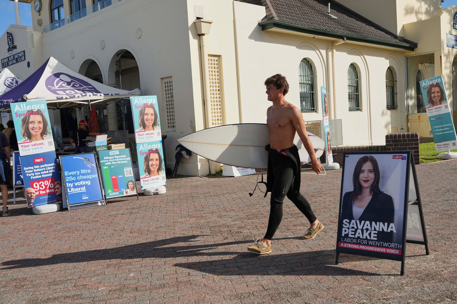 A surfer carries his board as he walks past a polling booth at Sydney's Bondi Beach, Saturday, May 3, 2025. (AP Photo/Mark Baker)