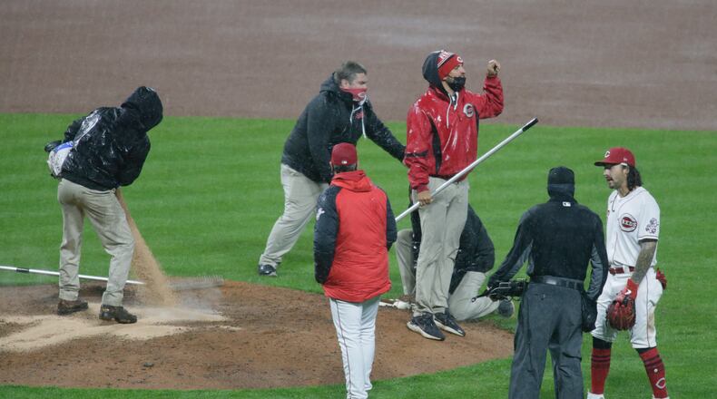 The Reds grounds crew works on the mound as manager David Bell, center, watches, just before the game was suspended by rain in the eighth inning on Tuesday, April 20, 2021, at Great American Ball Park in Cincinnati. David Jablonski/Staff
