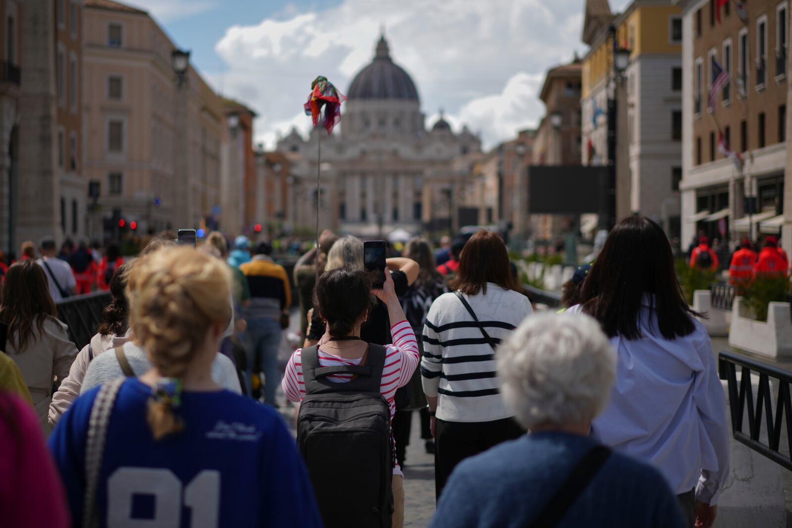 People walk along Via della Conciliazione avenue to line up to view Pope Francis lying in state inside St. Peter's Basilica, seen in the background, at the Vatican, Thursday, April 24, 2025. (AP Photo/Andrew Medichini)
