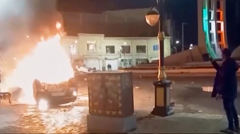 This frame grab from a video released Friday, Jan. 9, 2026, by Iranian state television shows a man holding a device to document burning vehicles during a night of mass protests in Zanjan, Iran. (Iranian state TV via AP)