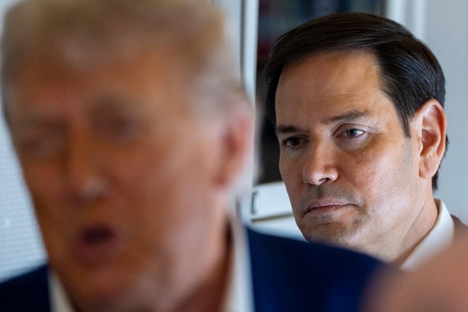 Secretary of State Marco Rubio stands behind as President Donald Trump speaks with reporters on Air Force One while in flight from Joint Base Andrews, Md., to Amsterdam, Netherlands, Tuesday, June 24, 2025. (AP Photo/Alex Brandon)