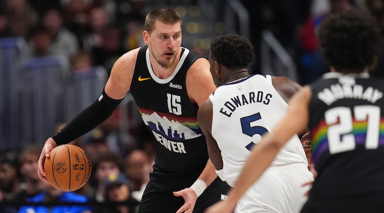 Denver Nuggets center Nikola Jokić, back, looks to pass the ball as Minnesota Timberwolves guard Anthony Edwards defends in overtime of an NBA basketball game Thursday, Dec. 25, 2025, in Denver. (AP Photo/David Zalubowski)