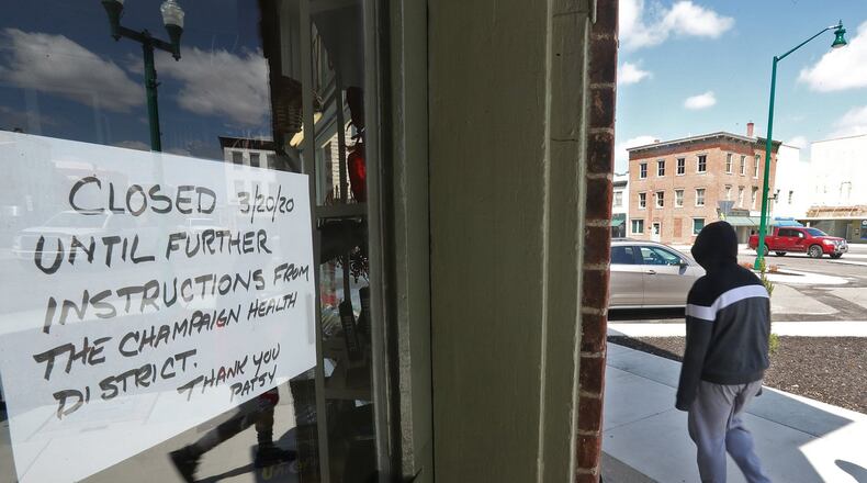 A pedestrian walks down the sidewalk past all the “Closed” signs on businesses in downtown Urbana in April as a statewide stay-at-home order was implemented due to the coronavirus pandemic. BILL LACKEY/STAFF