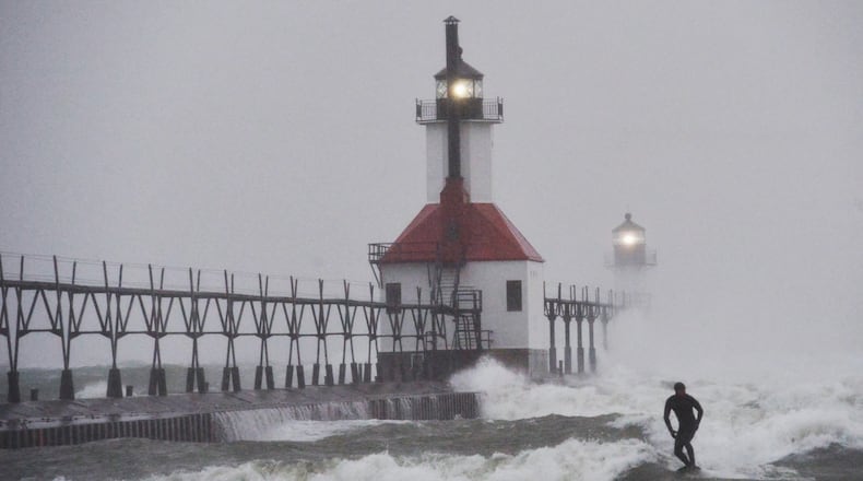 A surfer rides through blowing snow as Lake Michigan waves crash into the St. Joseph Inner and Outer Lighthouses Wednesday, Nov. 26, 2025, in St. Joseph, Mich. (Don Campbell/The Herald-Palladium via AP)