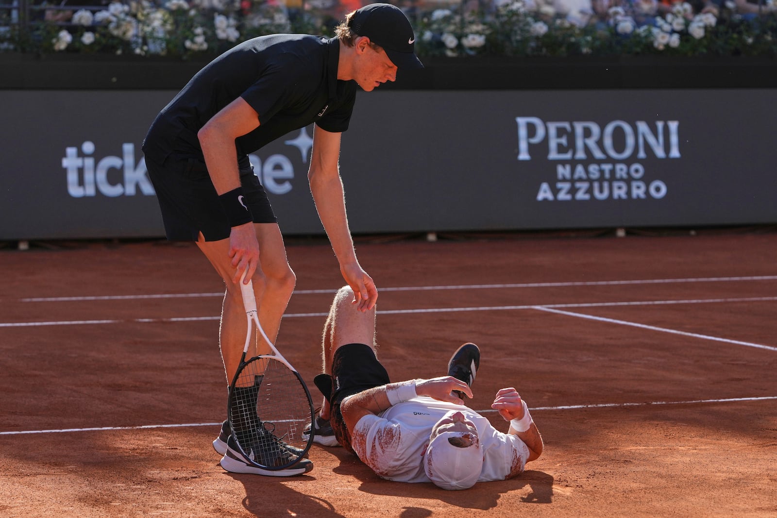 Italy's Jannik Sinner, standing, tends to Netherlands' Jesper De Jong who lies on the court after falling, during their tennis match at the Italian Open at the Foro Italico, in Rome, Monday, May 12, 2025. (AP Photo/Alessandra Tarantino)
