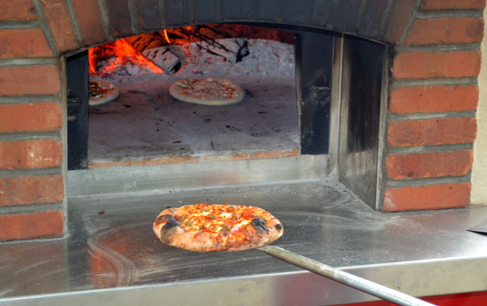 A finished Bella Sorella Pizza coming out of the mobile wood-fired brick oven. Photo by Mark Fisher