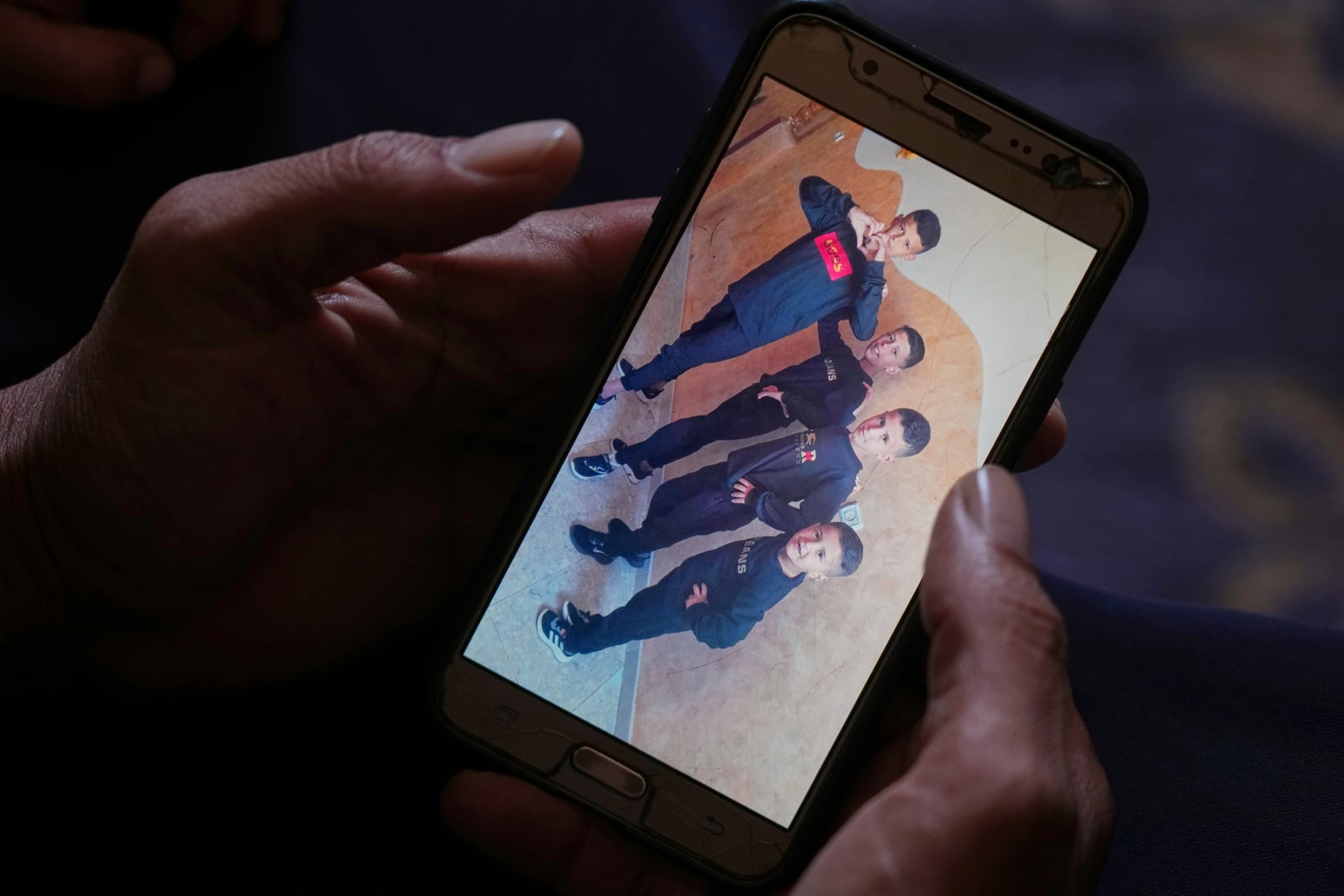 Hatem Al-Nouri shows a photo of his children Amir, 4, right, and Omar, 8, second from right, accompanied by their brothers, as he talks about when Hatem and Amir were killed in an Israeli strike while waiting to receive nutritional supplements at a medical clinic, during an interview at his home in Deir al-Balah, Gaza Strip, Friday, July 11, 2025. (AP Photo/Abdel Kareem Hana)