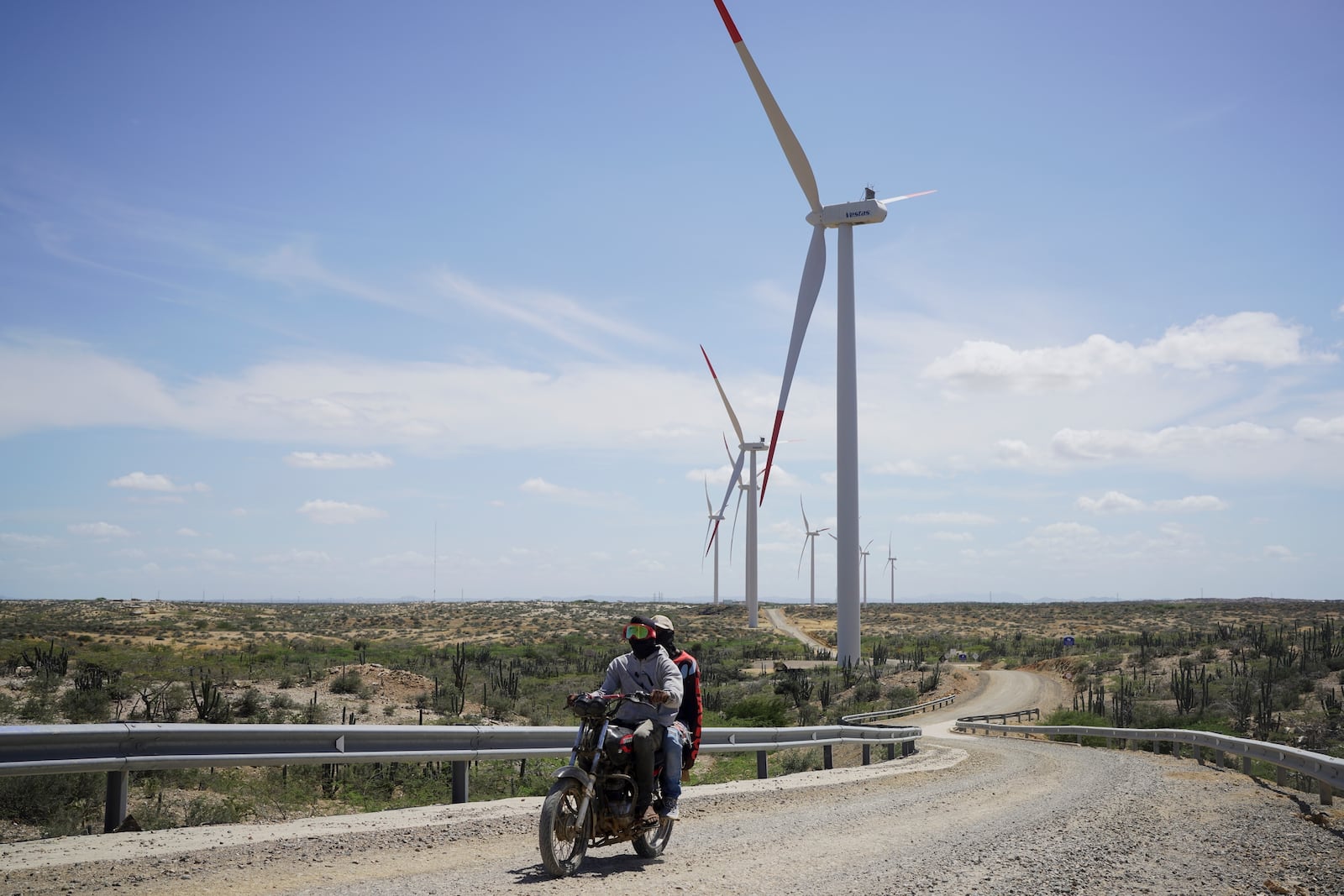 FILE - Two people on a motorcycle drive near wind turbines on the outskirts of Cabo de la Vela, Colombia, Feb. 7, 2025. (AP Photo/Ivan Valencia, File)