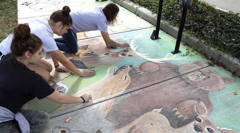 Cheyenne Combs, left, Ellie Shinkle, center, and Melissa Sherrock work on a chalk picture during Chalktoberfest at National Road Commons Park. Bill Lackey/Staff