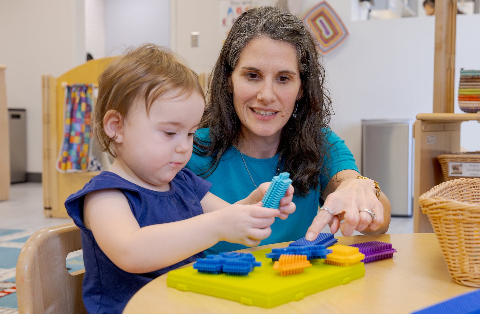 Nicole Myrick, director of Mini University at Sinclair Community College, explains a toy to a child on Tuesday, March 10. Child care providers have, had small profit margins, but new regulations have cut the amount of money the state reimbursed to childcare providers. BRYANT BILLING / STAFF