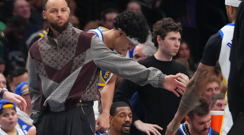 Golden State Warriors guard Stephen Curry wears street clothes while standing near his team's bench during a timeout against the Dallas Mavericks in the first half of an NBA basketball game Monday, March 23, 2026, in Dallas. (AP Photo/Julio Cortez)