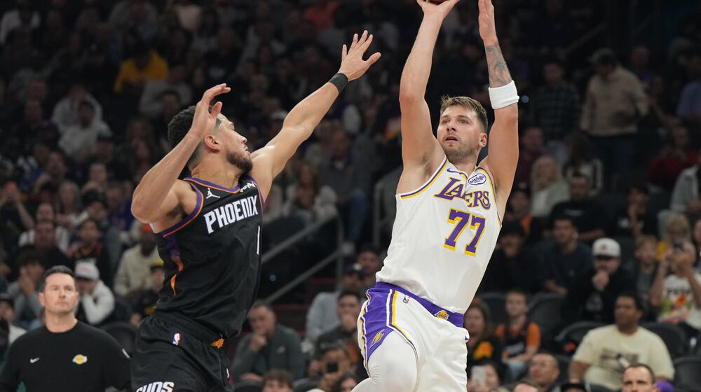 Los Angeles Lakers guard Luka Doncic (77)looks to shoot over Phoenix Suns guard Devin Booker, front left, during the first half of an NBA basketball game, Sunday, Dec. 14, 2025, in Phoenix. (AP Photo/Rick Scuteri)