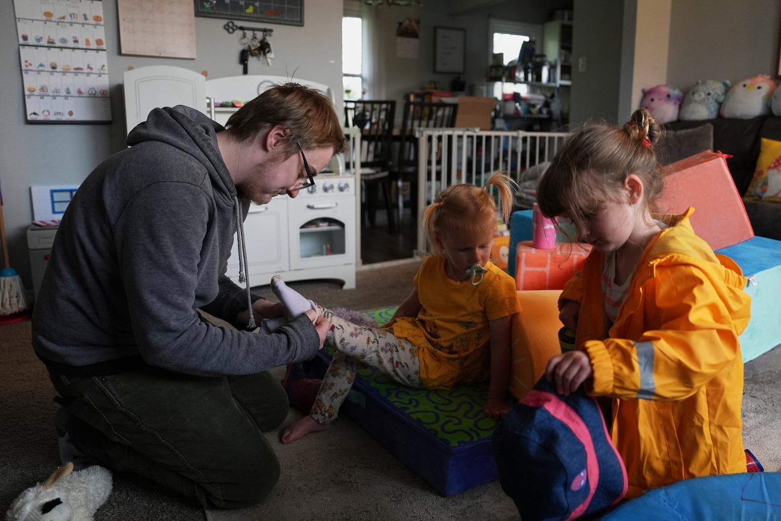 Kirt Ethridge, left, puts socks on his daughter, Naomi, 2, center, as his other daughter, Eliza, 5, gets a hat before a walk Thursday, April 10, 2025, in Evansville, Ind. (AP Photo/Joshua A. Bickel)