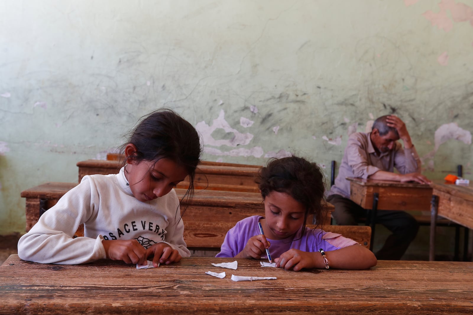 Displaced Bedouin girls who fled with their families from the town of Shahba in southern Sweida province due to clashes between Bedouin clans and Druze militias, draw on scraps of paper inside a classroom turned shelter in the town of Nahtah, in the eastern part of Daraa province, Syria, Monday, July 21, 2025. (AP Photo/Omar Sanadiki)