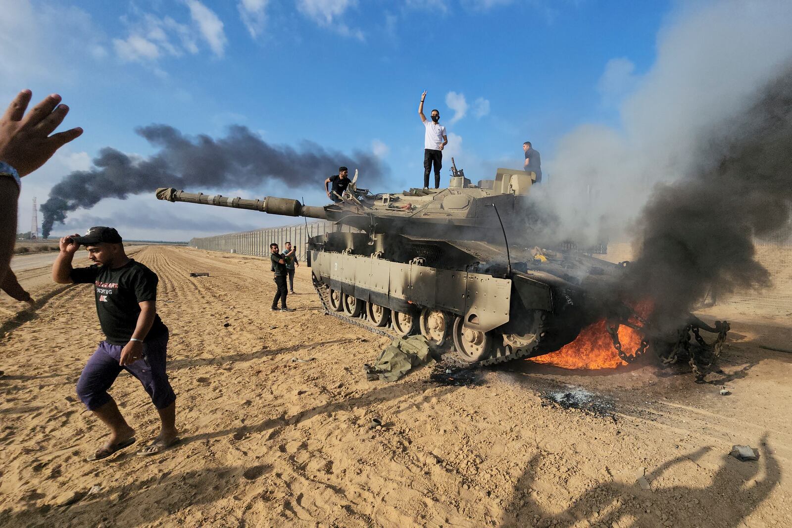 FILE - Palestinians celebrate by a destroyed Israeli tank at the border fence between Israel and the Gaza Strip, east of Khan Younis, during a surprise attack on Israel, Saturday, Oct. 7, 2023. (AP Photo, File)