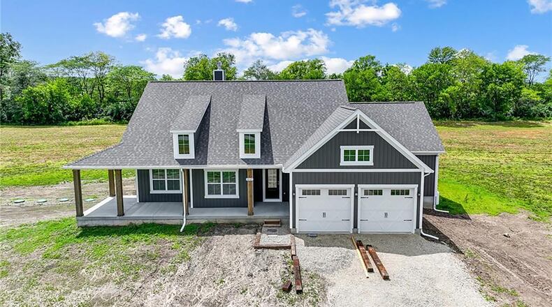 The front of the new construction ranch home has a covered wrap around porch and decorative dormers. It also has a two car attached garage.