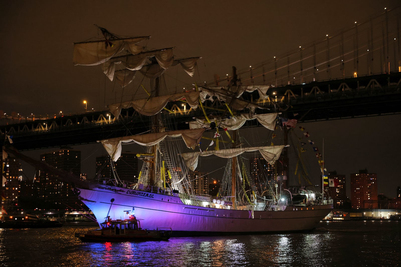 A New York Police Department harbor unit passes in front of the Cuauhtémoc, a masted Mexican Navy training ship as it sits stranded near the Manhattan Bridge after colliding with the Brooklyn Bridge, Saturday, May 17, 2025, in New York. (AP Photo/Yuki Iwamura)