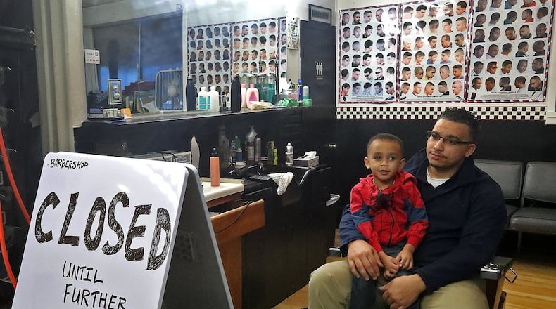 Alex Robinson, owner of Robinson Corner Cuts, and his son, Jarred, sit in his empty barber shop Thursday after the governor ordered all barber shops and nail salons to close Wednesday due to the coronavirus. BILL LACKEY/STAFF