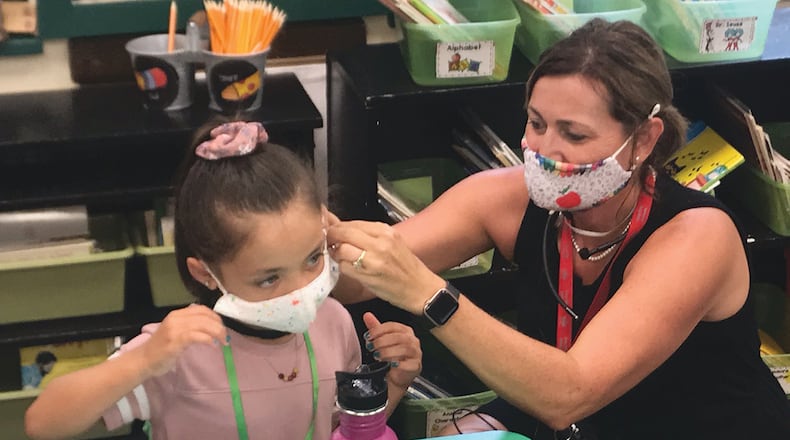 Heywood Elementary School first-grade teacher Angela Laird (right) helps student Madalyn Lee adjust her face mask Tuesday on the Troy City Schools' first day of both in-person and online learning.