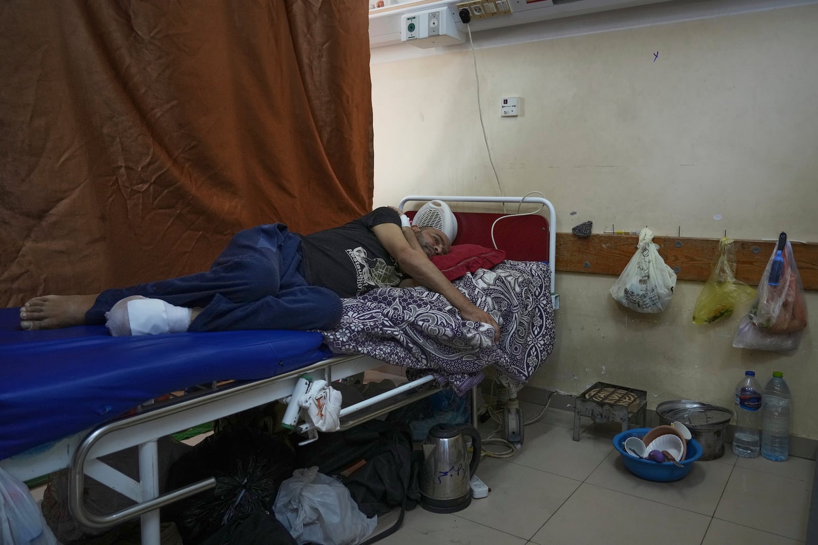 Sobhi al-Bursh, who was injured in a bombing and lost his foot, lies in bed next to dishes and a portable electric stove used to cook food brought from home at Nasser Hospital in Khan Younis, Gaza Strip, Tuesday, May 6, 2025. (AP Photo/Abdel Kareem Hana)