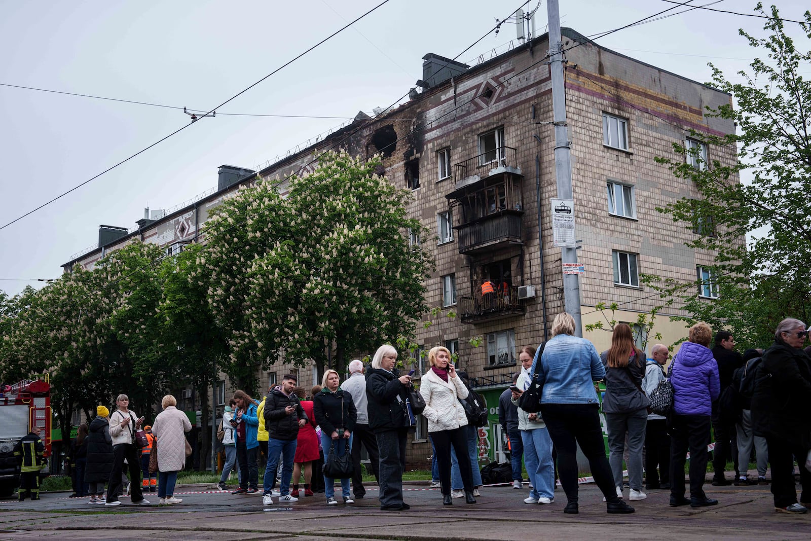 Local residents wait for a tram in front of a residential building, damaged after a Russian strike, in Kyiv, Ukraine, on Wednesday, May 7, 2025. (AP Photo/Evgeniy Maloletka)