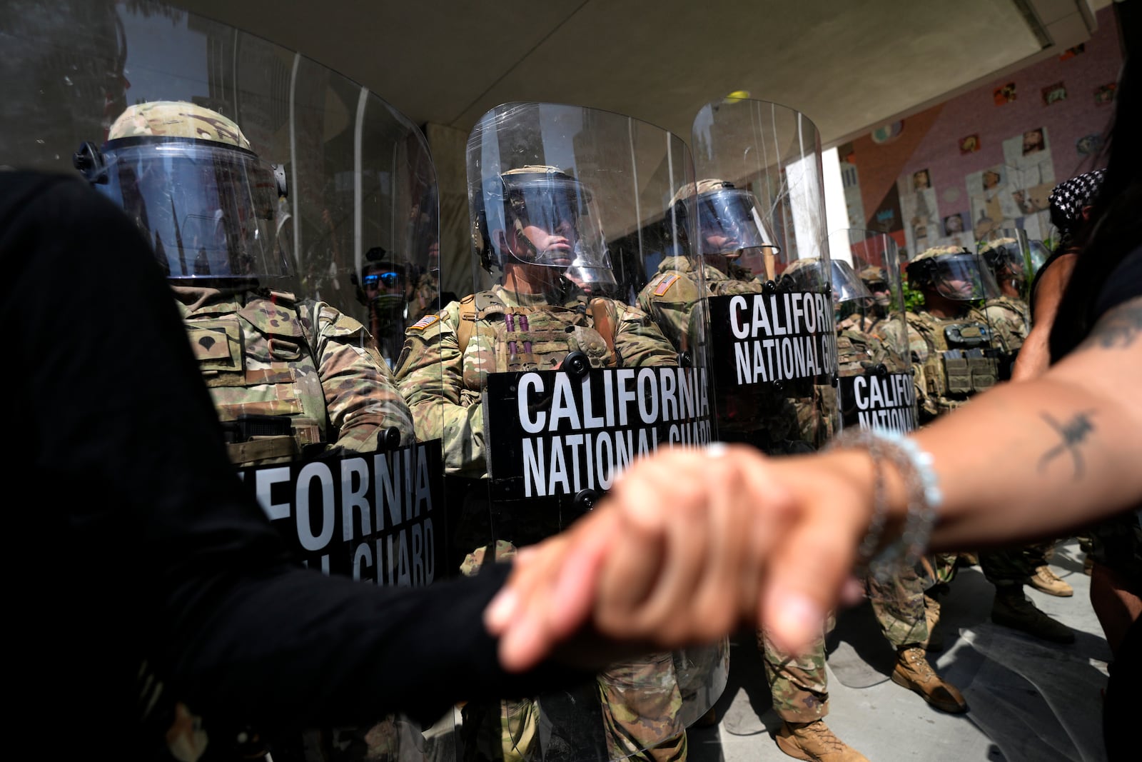 Protesters clasp hands in front of a line of California National Guard, Monday, June 9, 2025, at a Federal Building in downtown Los Angeles. (AP Photo Jae Hong)
