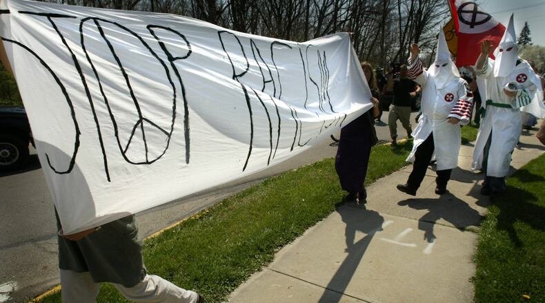 Hooded and robed members of the Ku Klux Klan walk down a sidewalk in Yellow Springs to protest racial discrimination against whites in 2004. Protesters to their appearance, meanwhile, carry a “stop racism” sign. The event was without arrests. STAFF/FILE