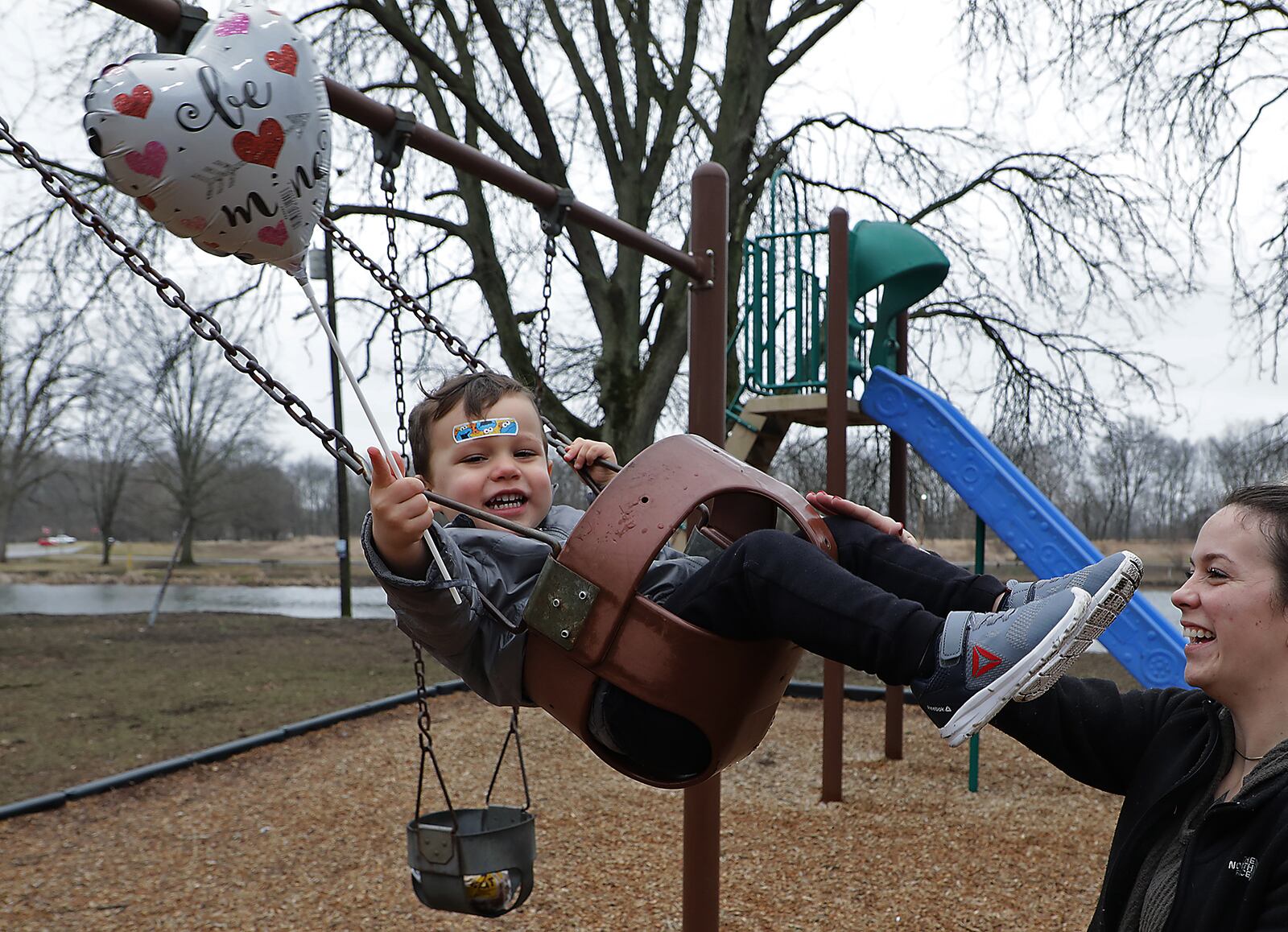 Callan Bowling, 2, holds a Valentine's Day ballon as he and his mother, Hayley Rowland, go for a swing at Old Reid Park Tuesday between rain showers. BILL LACKEY/STAFF
