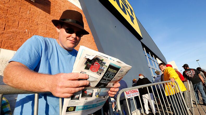 Josh Vanderpool reads the sale ads as he waits in line outside Best Buy in Springfield on Thanksgiving day. Several hundred people were waiting in line when the doors opened at 5 p.m. Thursday. Bill Lackey/Staff